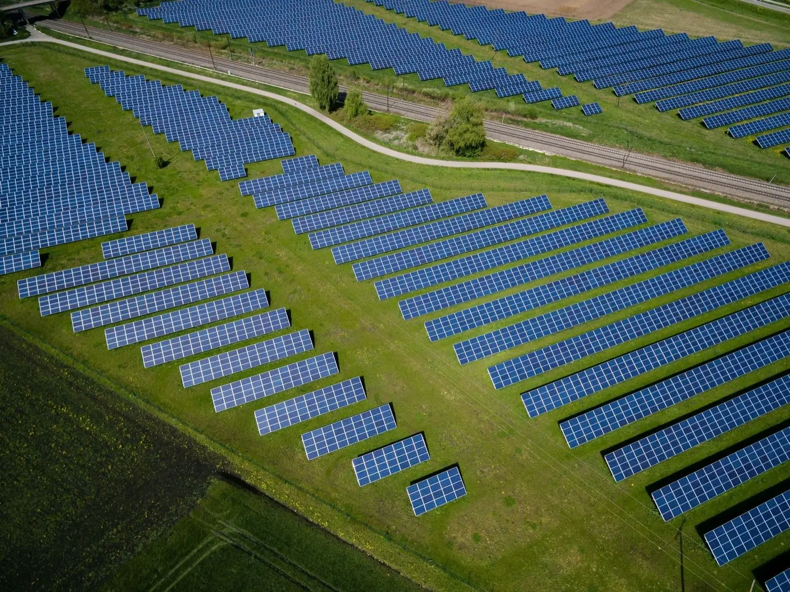 Aerial view of long rows of dark blue solar panels covering a green field.