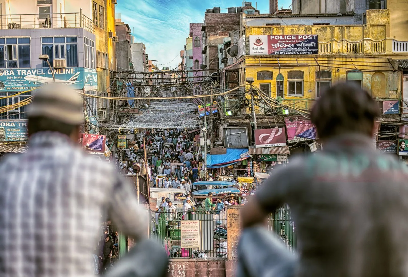 Shoppers and vendors packed into a narrow street market in Delhi, with goods stacked along both sides.