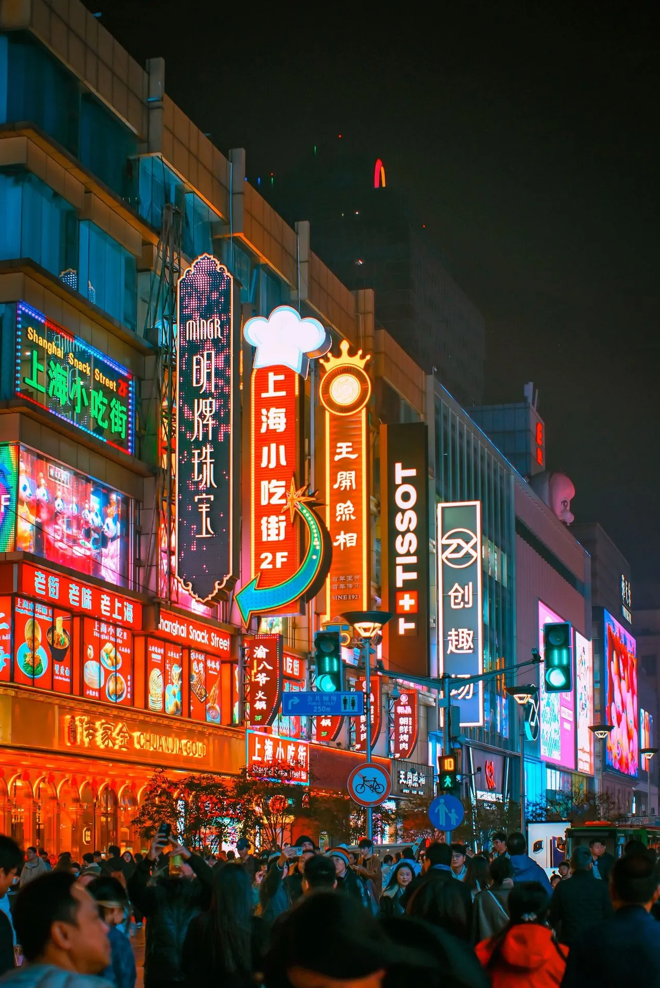 Pedestrians filling a brightly lit shopping street in Shanghai at night, with neon signs above the crowd.